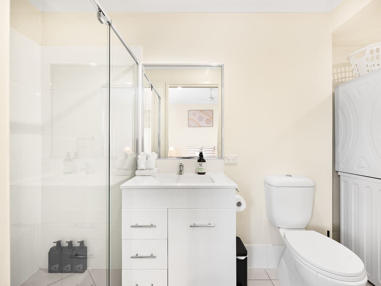 Een moderne badkamer met een douchecabine van glas, een wit wastafelmeubel met een spiegel erboven en een toilet.