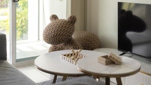 A modern living room with a large TV, a round coffee table, and a sofa with a bear-shaped pillow. - Walk to everything! Modern 2Beds Apt w/ EasyAccess (Springwood)