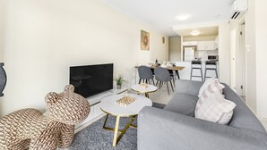 A modern living room with a grey sofa, a TV, and a dining area with chairs and a table. - Walk to everything! Modern 2Beds Apt w/ EasyAccess (Springwood)