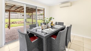 A dining area with a table set for four, surrounded by wicker chairs with red cushions. - 3Beds Vibrant Home Steps to Mall & Transport (Sunnybank)
