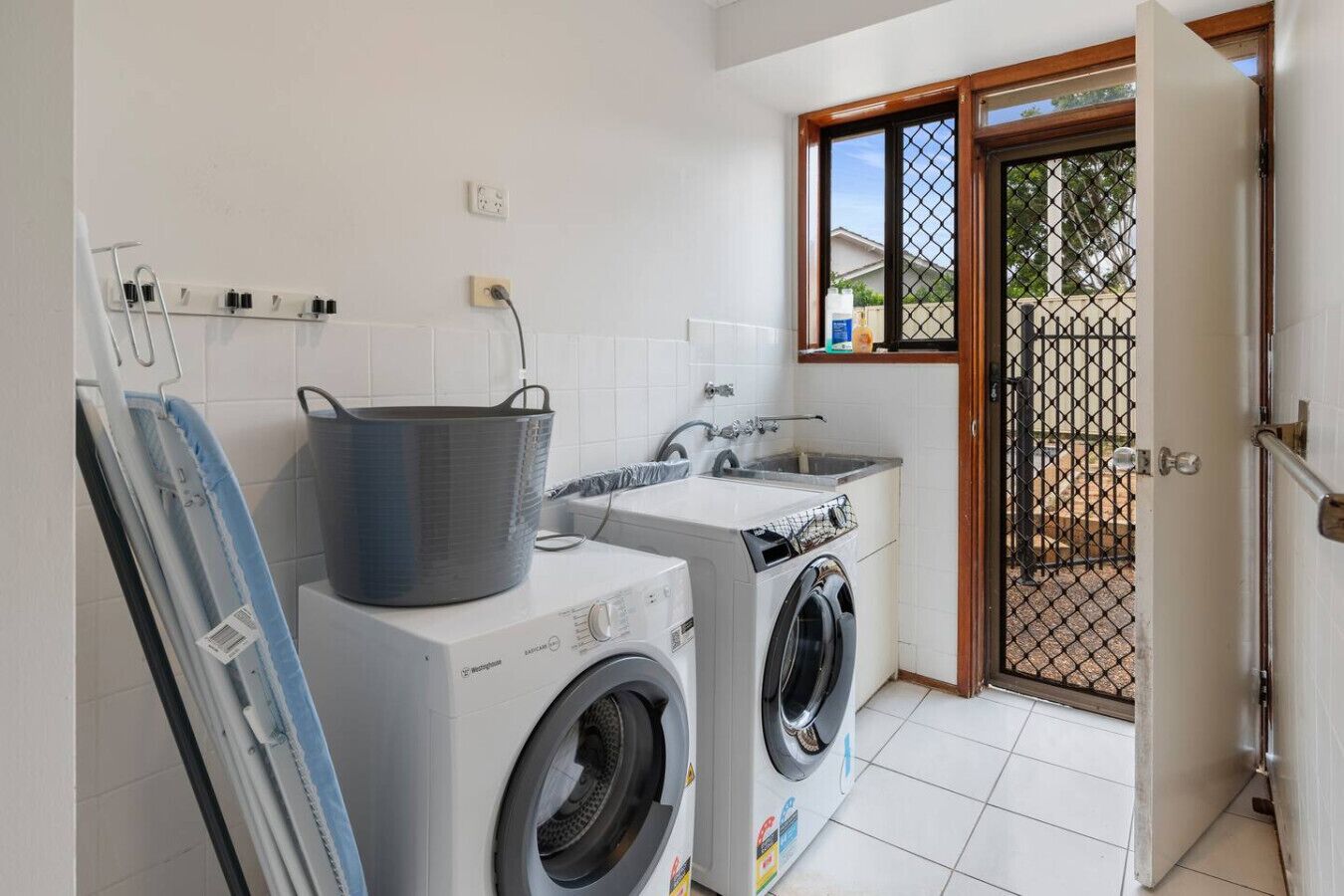 A compact laundry room with a washing machine, dryer, and ironing board.