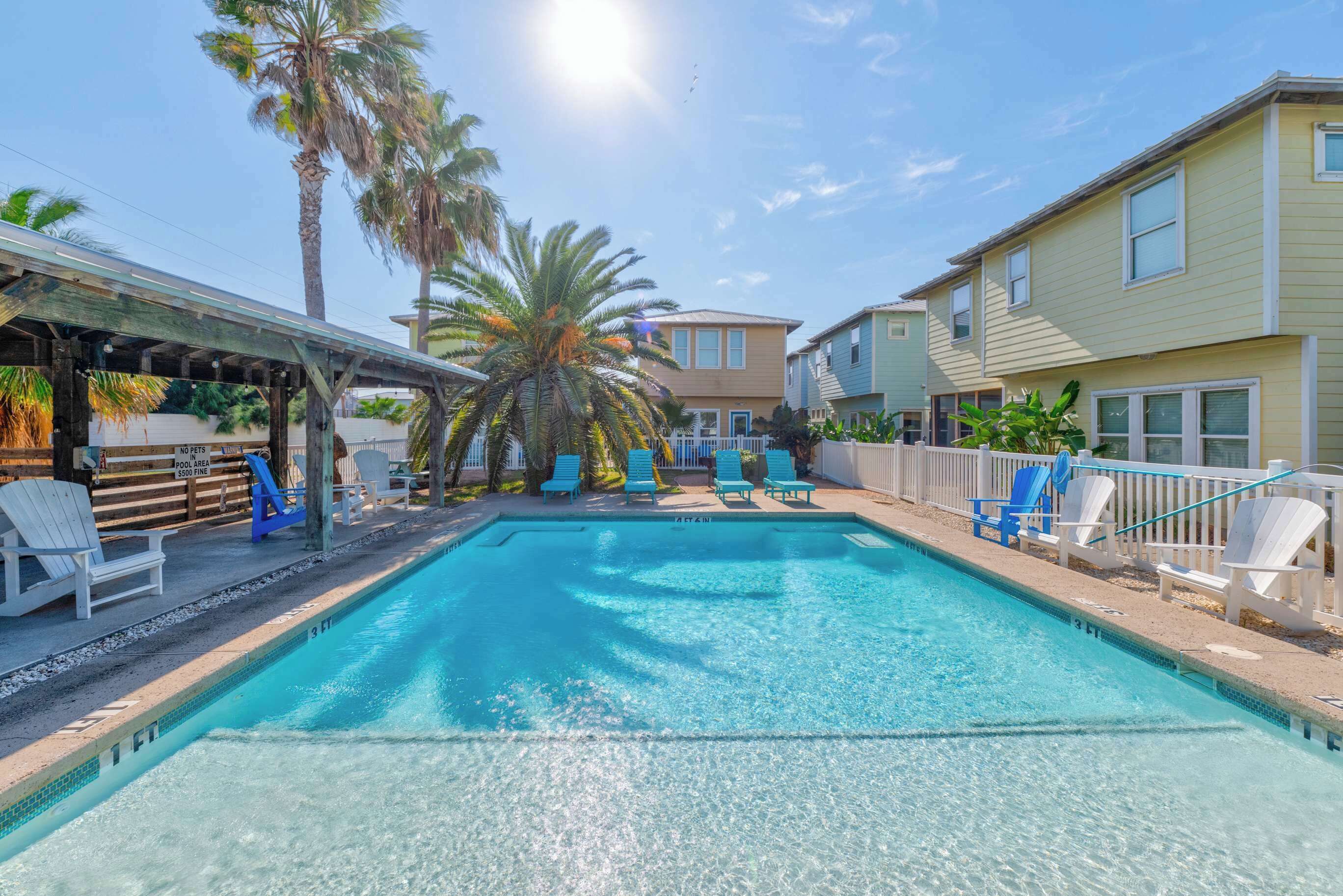 A swimming pool with lounge chairs, palm trees, and a covered area.