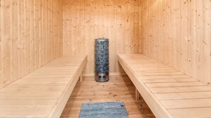 A sauna room with wooden walls and benches, a central heater, and a blue mat on the floor. - "Kerttuli" - 540m from the sea by Interhome (Væggerløse)