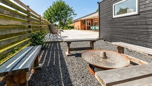 An outdoor patio area with wooden benches and tables, a pergola, and a view of a brick building in the background. - "Kerttuli" - 540m from the sea by Interhome (Væggerløse)