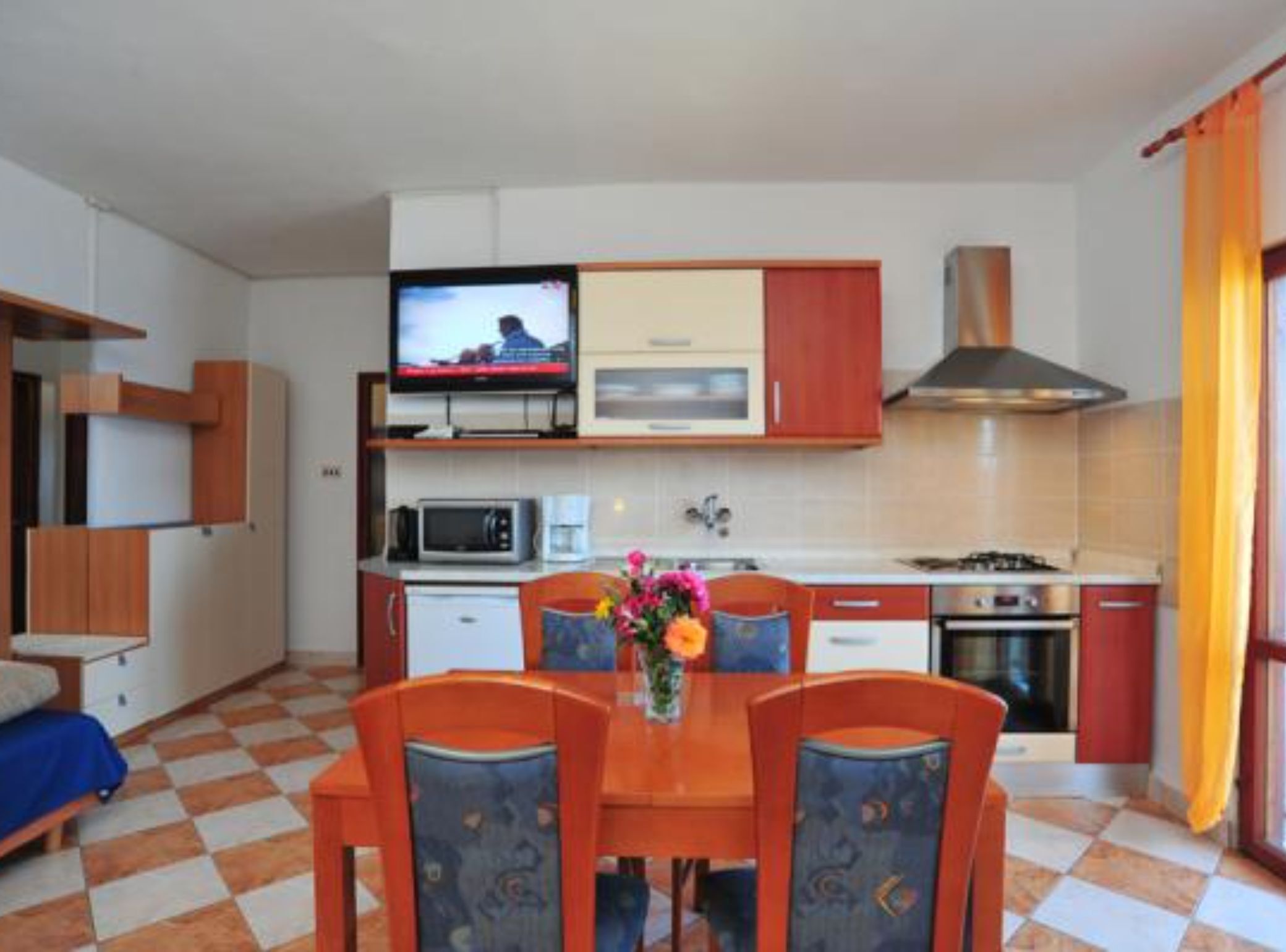 Cuina compacta amb televisió, microones i fogó. Hi ha una taula de dinar amb cadires i un sofà petit.