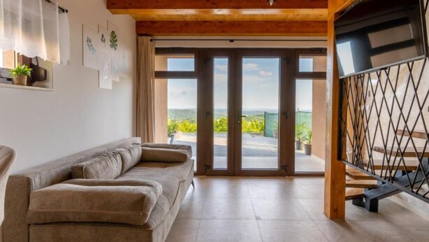 Ein geräumiges Wohnzimmer mit Holzboden, einem Sofa und einer großen Schiebeglastür, die auf eine Außenterrasse führt.