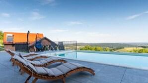 Ein Pool mit Liegestühlen, einem Whirlpool und Blick ins Grüne.