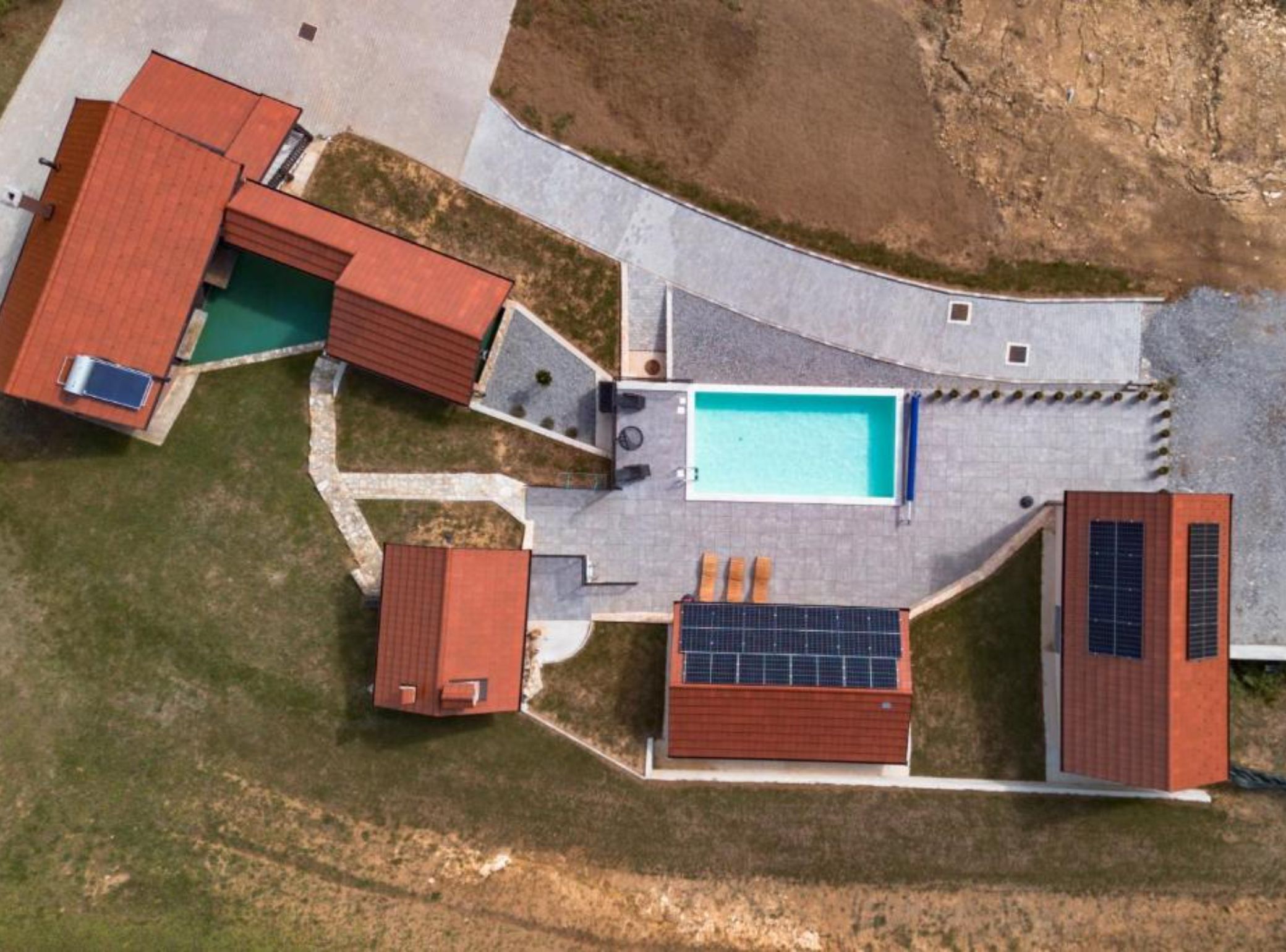 An aerial view of a residential property with a swimming pool, solar panels, and a covered patio area.