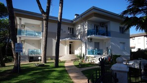 A two-story building with a balcony, a sign indicating it is a hotel, and a well-maintained lawn. - Fully equipped flat in a pinewood area with pool (Lignano Sabbiadoro)