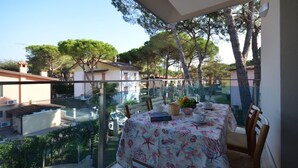 A balcony with a table set for dining, overlooking a residential area with trees and houses. - Spacious and familiar flat (Lignano Sabbiadoro)