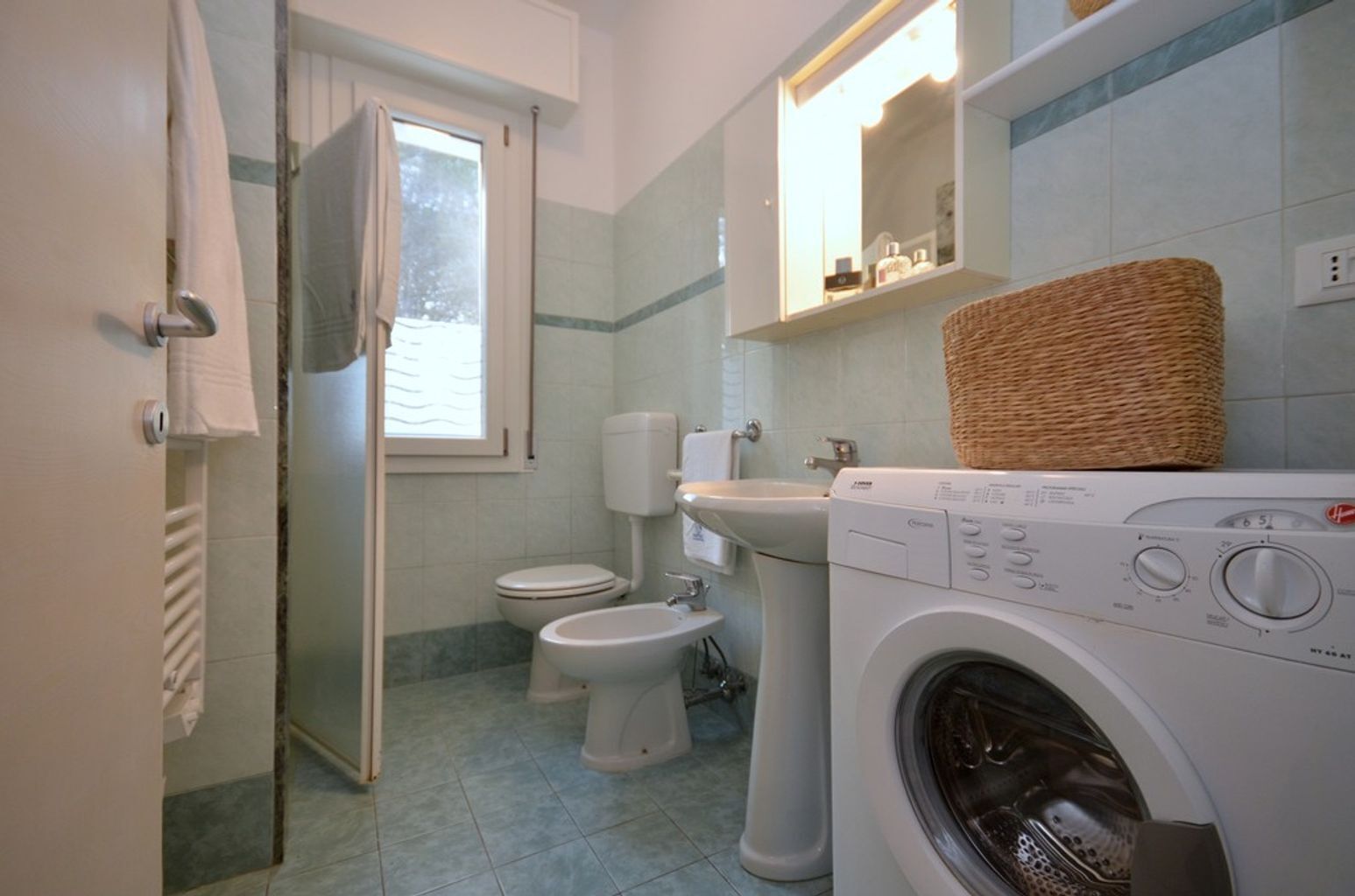 A bathroom with a washing machine, two toilets, a sink, and a window.