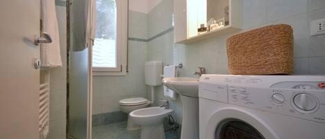 A bathroom with a washing machine, two toilets, a sink, and a window.