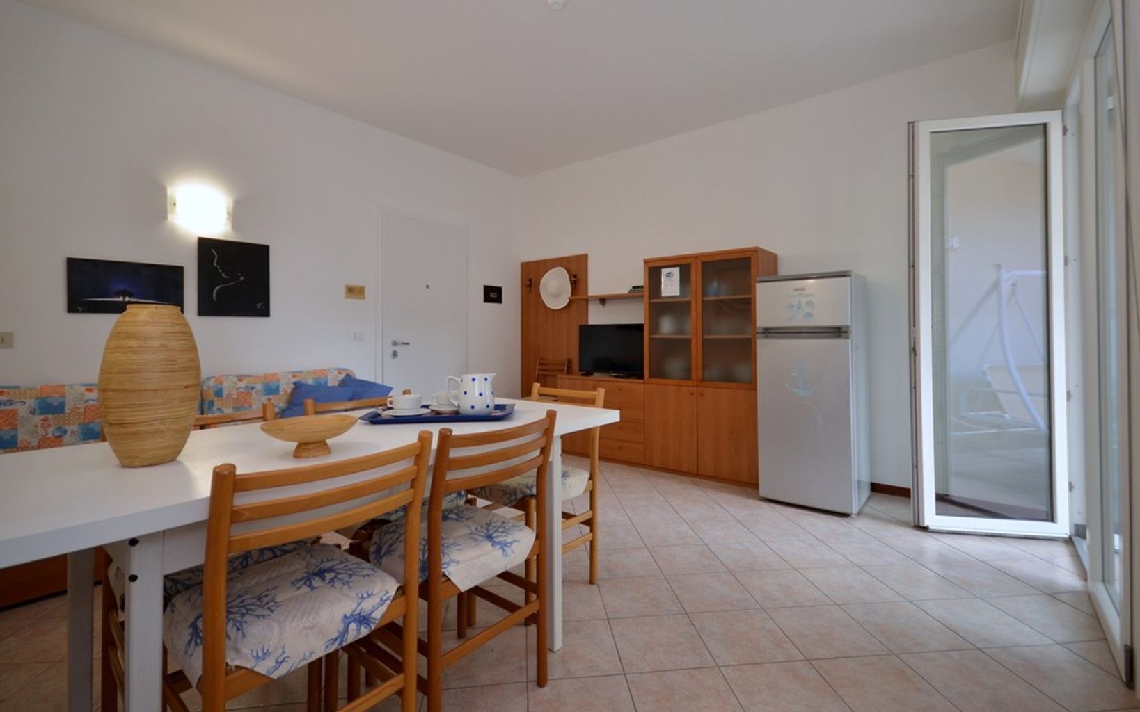 A compact kitchen with a dining table, chairs, a refrigerator, and wooden cabinets.
