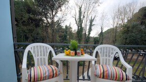 A balcony with two white chairs and a small table, featuring a striped cushion and a potted plant with flowers.