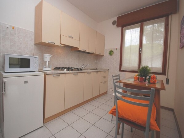 A compact kitchen with a microwave, stove, and sink. There is a dining table with chairs and a window with curtains.