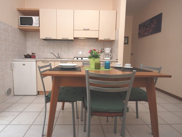 A compact kitchen with a dining table, chairs, a microwave, a refrigerator, and a coffee maker.