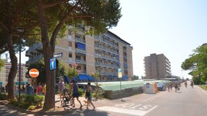A multi-story hotel with balconies, a parking area, and a pedestrian crossing. - Cozy apartment in an unbeatable location (Bibione)