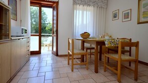 A dining area with a table set for two, wooden chairs, a bowl of fruit, and a microwave on a cabinet. - Downtown apartment by the beach (Bibione)