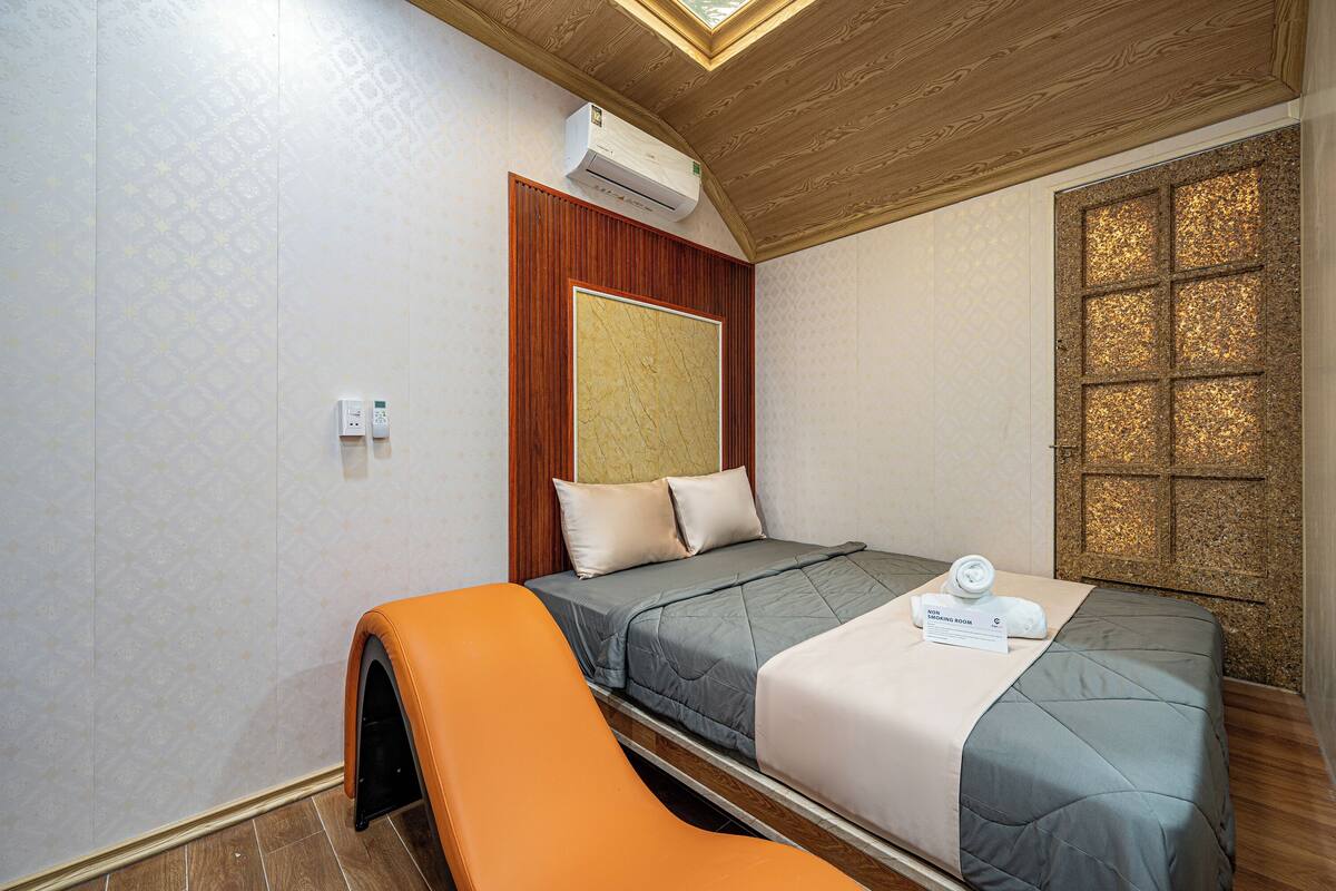 A hotel room with a bed, an air conditioning unit, a wooden ceiling, and a window with a decorative pattern.