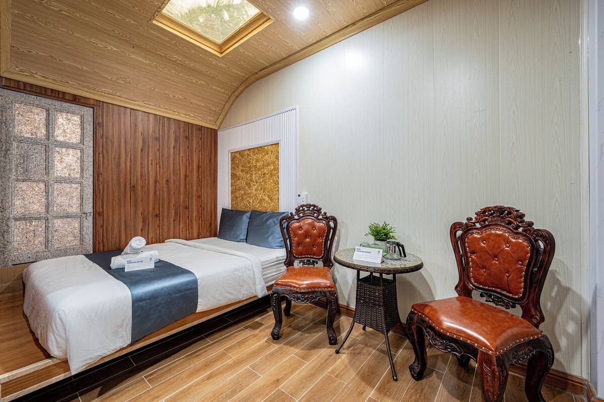 A hotel room with a bed, two chairs, a small table, and a window with a view.