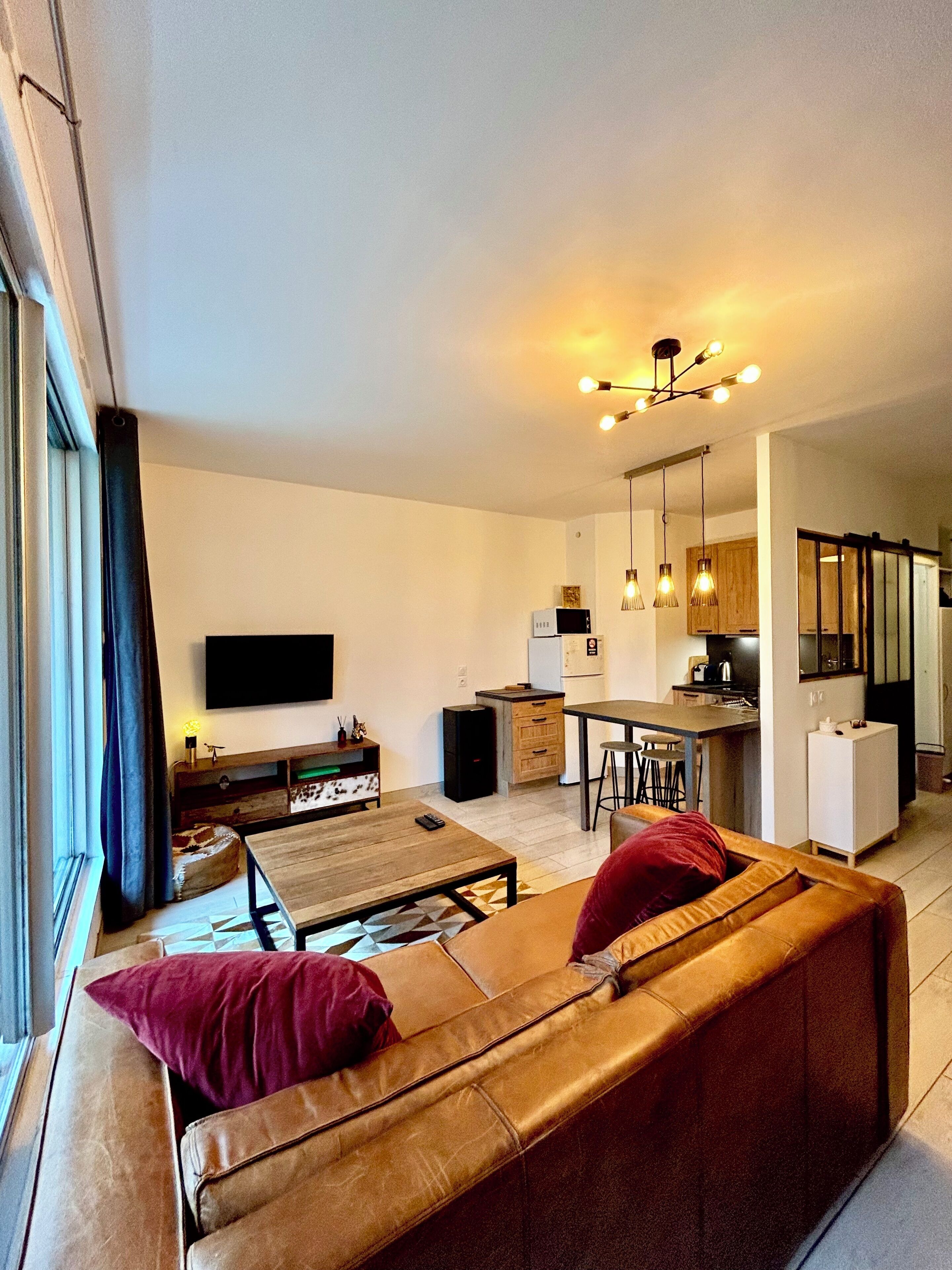 Ein modernes Wohnzimmer mit Sofa, Couchtisch und Fernseher. Eine Küchenzeile mit Esstisch und Stühlen ist ebenfalls vorhanden.