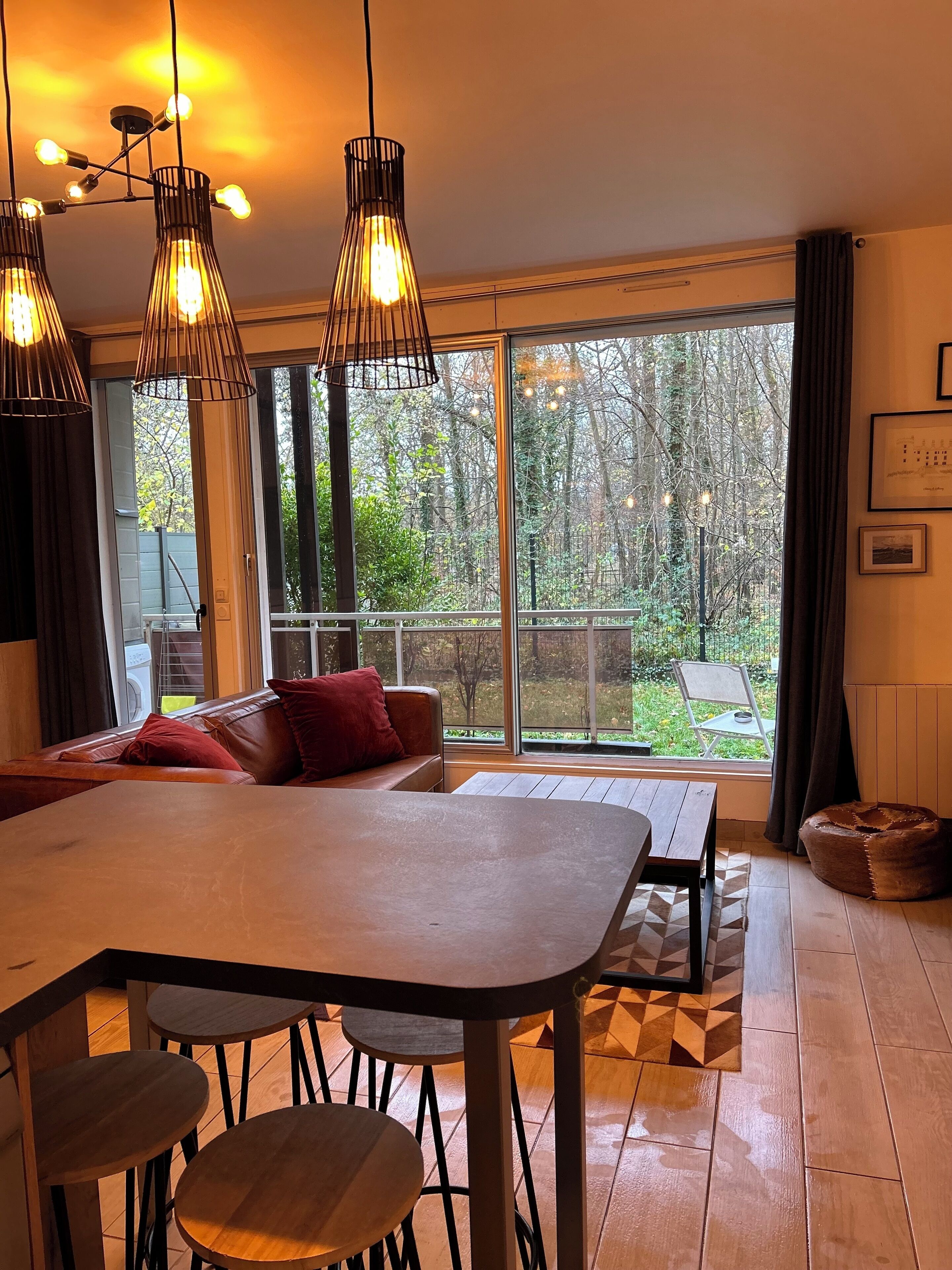 A modern dining area with a large table and chairs, a bench, and a view of a garden through large windows.