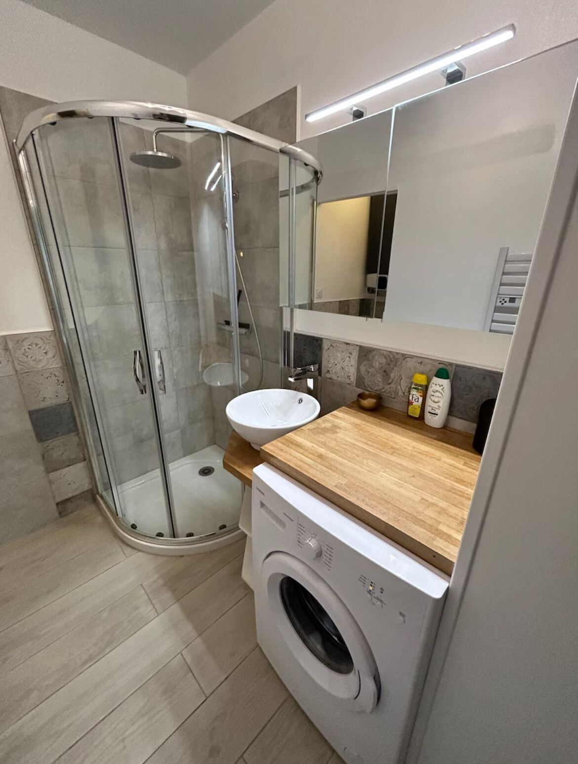 Een moderne badkamer met een glazen douchecabine, een wastafel, een spiegel en een wasmachine.