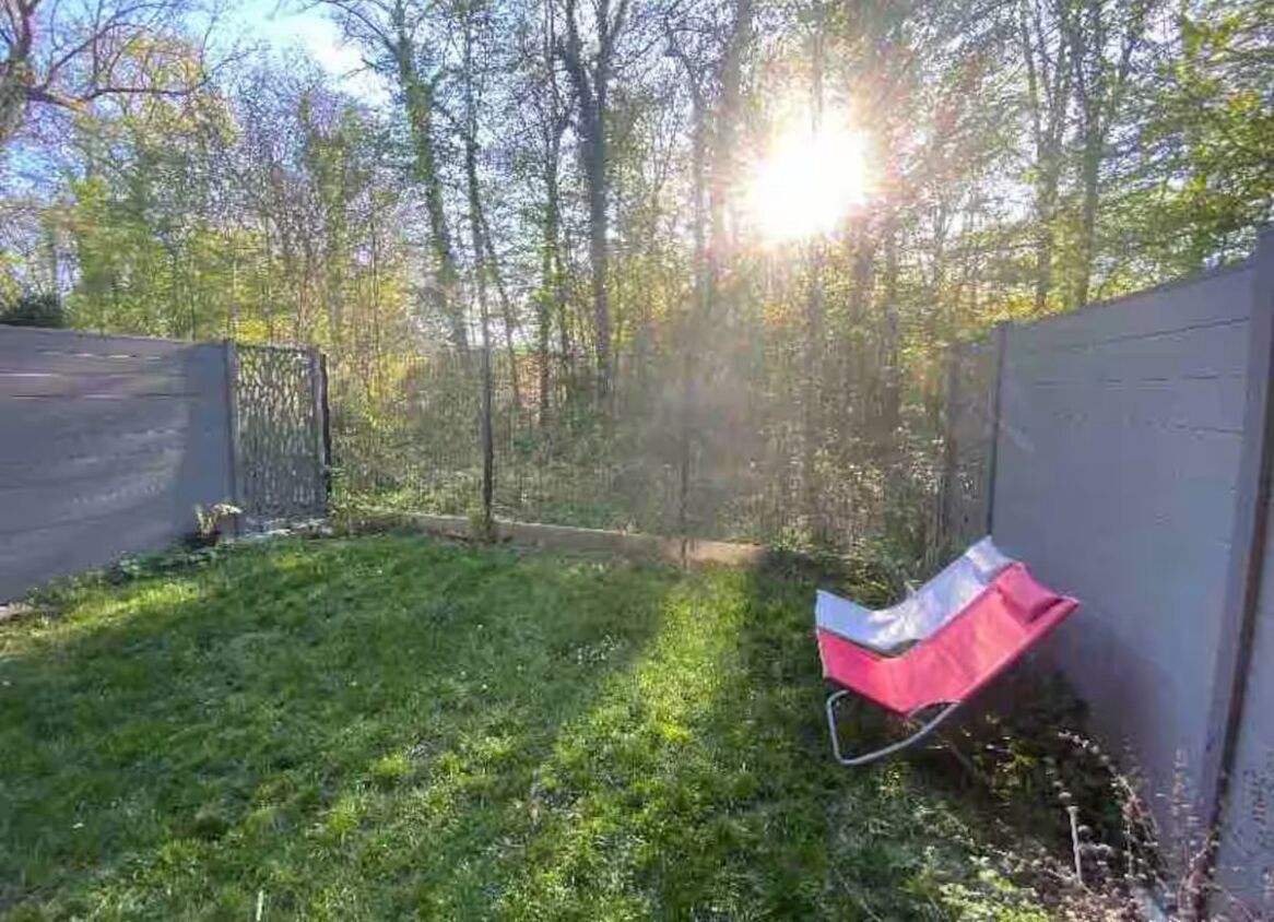 Un jardin avec une pelouse verdoyante, une chaise rouge et une clôture en bois.