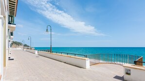 Ein gepflasterter Promenadenweg mit Geländer, der auf ein klares, blaues Meer blickt, ein Lampenpfahl und ein Gebäude mit Balkon.