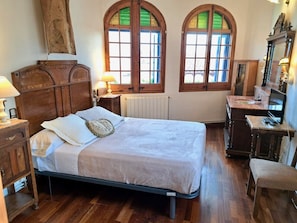 A bedroom with a bed, wooden dresser, desk, and arched windows. - HomeHolidaysRentals Suria - Costa Barcelona (Sant Pol de Mar)