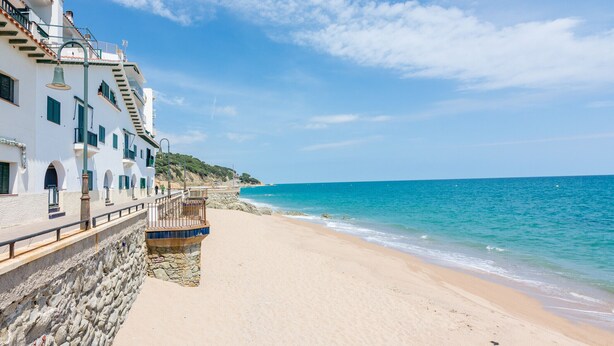 Ein Küstengebäude mit einer Steinmauer, einem Balkon und Blick auf Strand und Meer.