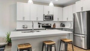 Una cocina moderna con armarios blancos, electrodomésticos de acero inoxidable, una isla grande con taburetes e iluminación colgante.