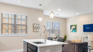 A modern kitchen with a central island, two pendant lights, and a view of the city through large windows.