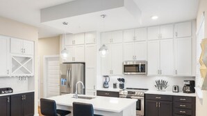 Une cuisine moderne avec des armoires blanches, des appareils en acier inoxydable et des luminaires suspendus.