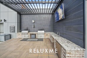 An outdoor kitchen area with two grills, a sink, and a brick backsplash.