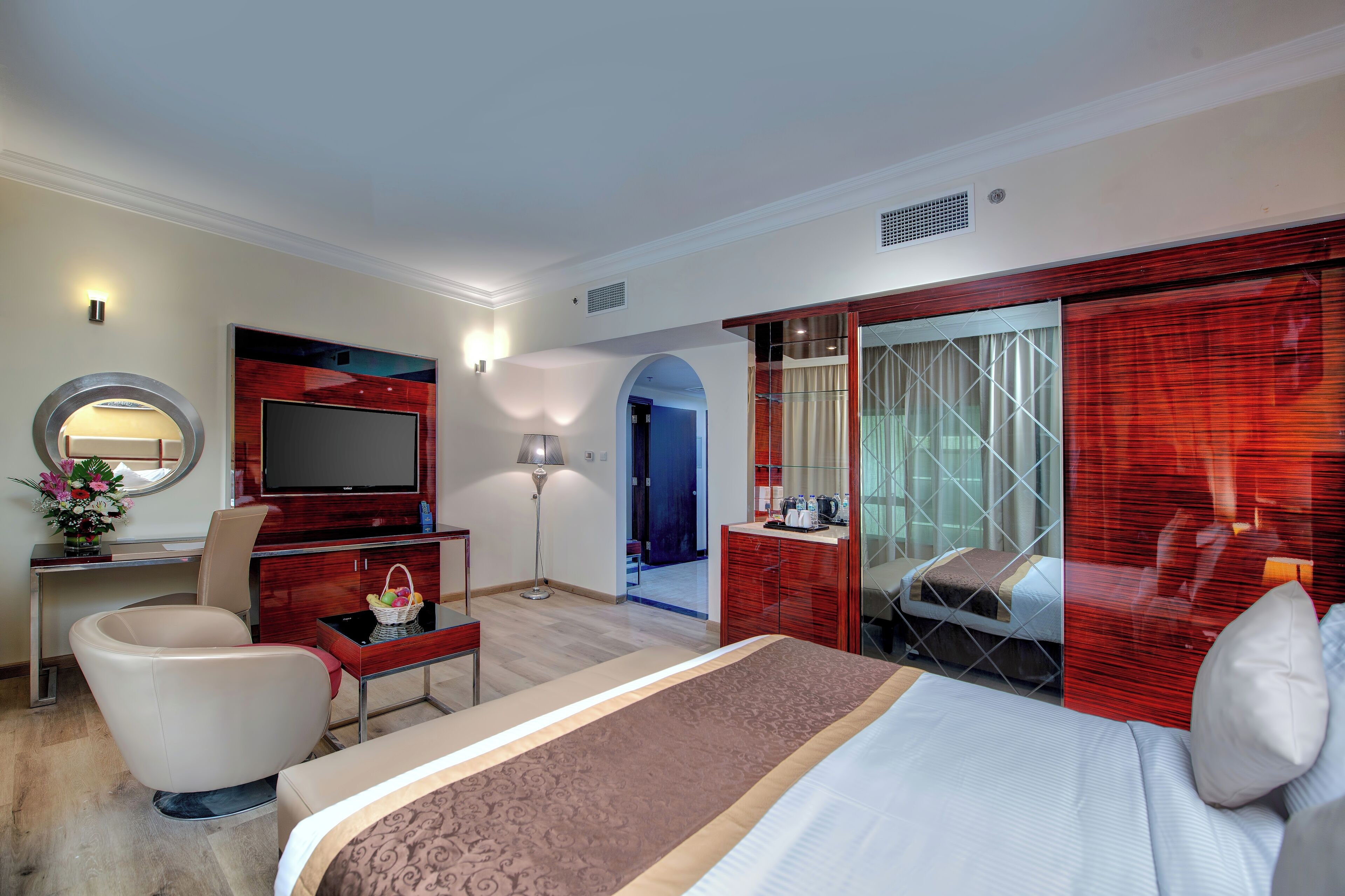 A hotel room with a bed, a desk, a TV, a chair, a mirror, and a wardrobe.