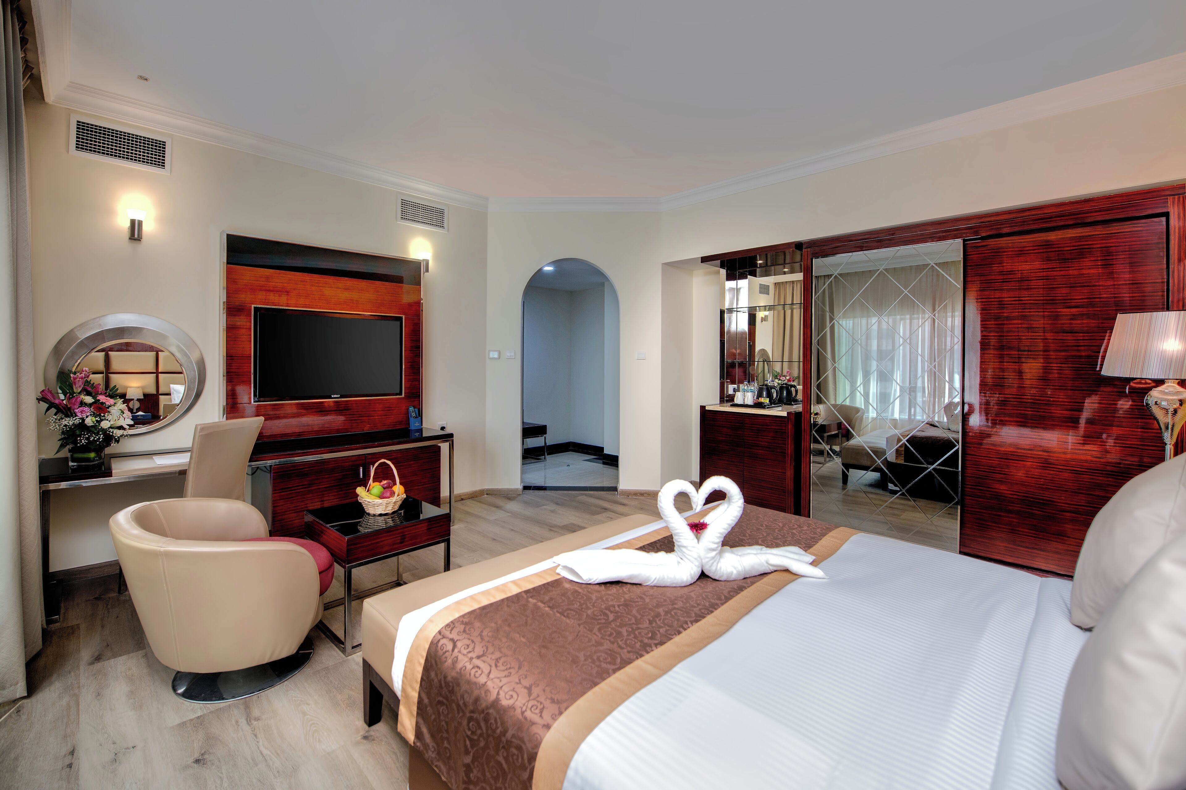 A hotel room with a large bed, a TV, a desk with a chair, and a mirror.