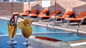 Zona de piscina con sillones de descanso y dos bebidas sobre una mesa.