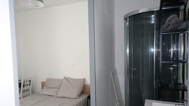 A bedroom with a bed, a white chair, a small table, and a shower area with a glass door. - Nice apartment in the center of Touraine, in the heart of the Loire castles (L'Île-Bouchard)