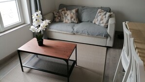 A living room with a grey sofa, patterned cushions, a wooden coffee table, and a vase of white flowers. - Nice apartment in the center of Touraine, in the heart of the Loire castles (L'Île-Bouchard)