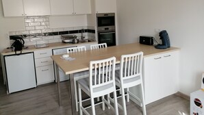 A modern kitchen with white cabinets, a wooden dining table, and a coffee machine. - Nice apartment in the center of Touraine, in the heart of the Loire castles (L'Île-Bouchard)