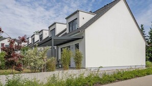 A modern building with a sloped roof, a covered outdoor area, and a garden with various plants.