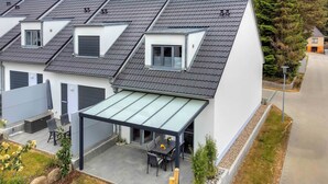 A modern residential building with multiple roof levels, a covered patio with outdoor furniture, and a small window.