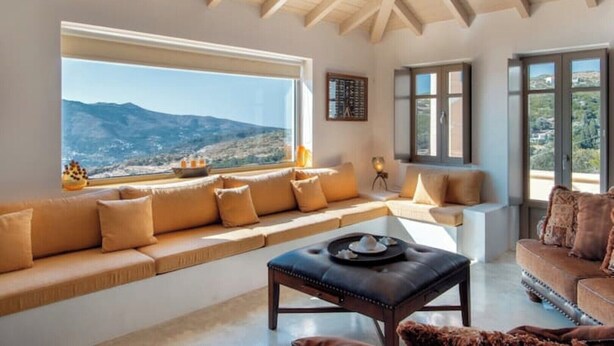 Una sala de estar con un ventanal grande, un sofá, una mesita de centro y vistas a montañas.