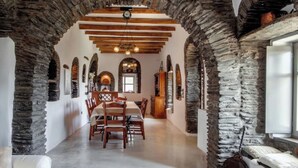 Un comedor con un arco de piedra, vigas de madera y una araña.