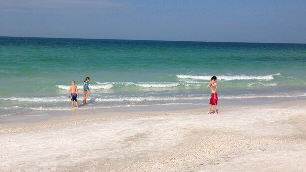 Una playa con tres personas caminando por la orilla.