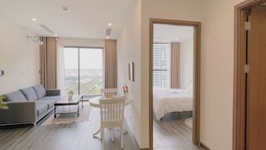 A modern living room with a sofa, a dining table, and a view of the city through large windows. - 1BR 12FL-Vinhomes Ocean Park Ha Noi (Hanoi)