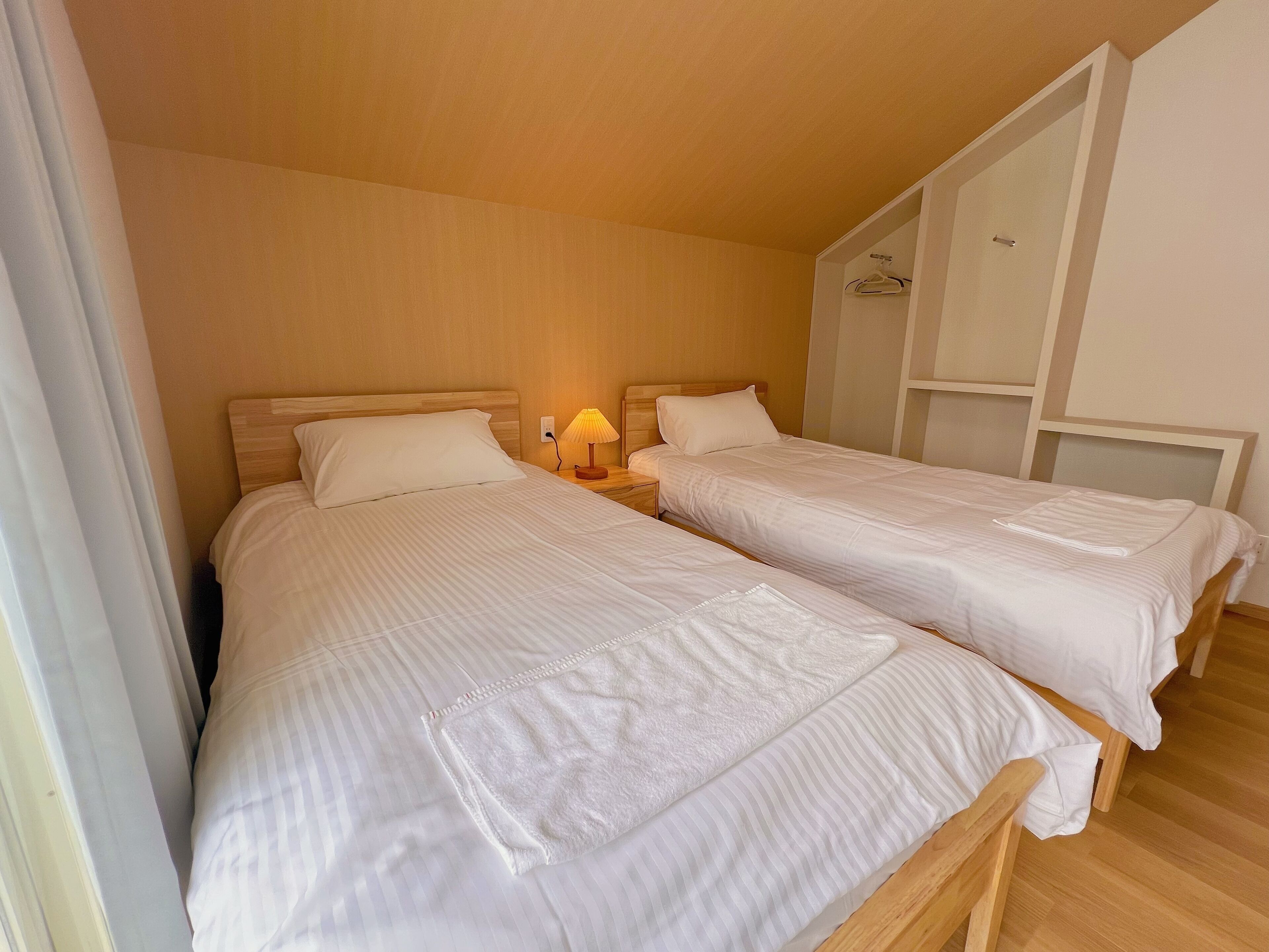Habitación de hotel con dos camas individuales, cabeceros de madera, una lámpara de noche y un armario.