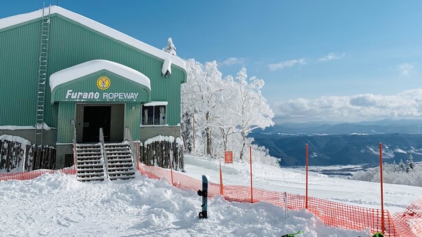 A green building labeled "Furano Ropeway" with a snowy landscape and mountains in the background. - Snowball Hostel (Furano)
