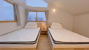 A room with two beds, a nightstand with a lamp, a window with curtains, and a view of the outside. - Snowball Hostel (Furano)